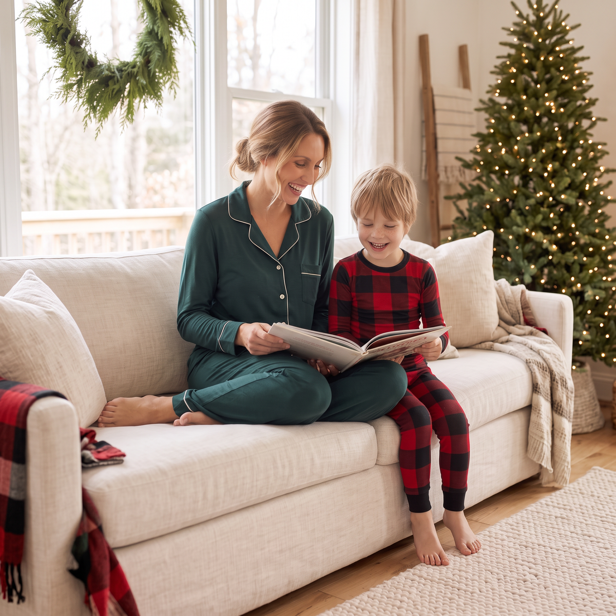 Mother wearing Balsam Women's Bamboo Button-Down Lounge Set reading a holiday storybook with her son in Canadian Plaid Bamboo PJs