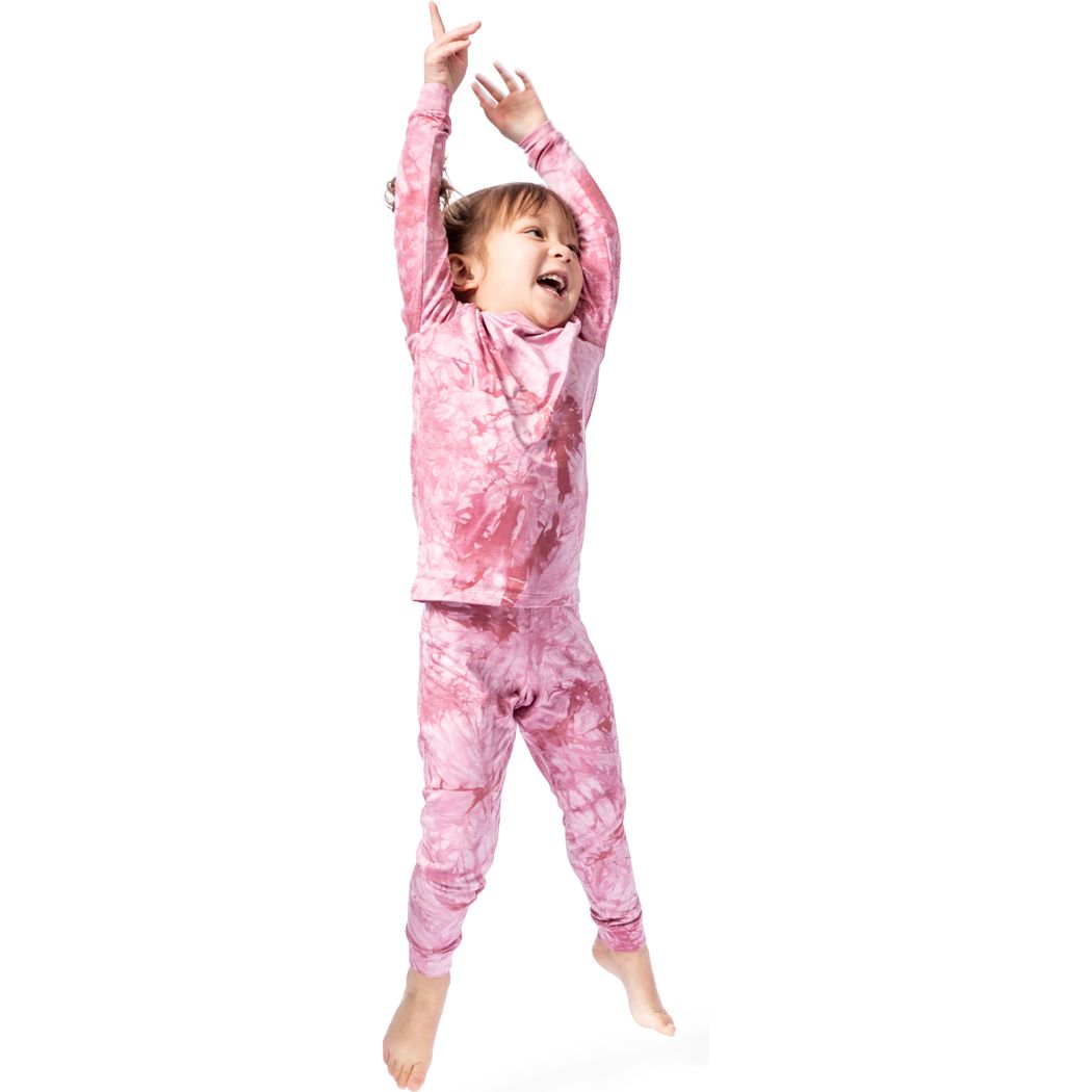 Child wearing pink tie-dye pajamas jumping on a white background