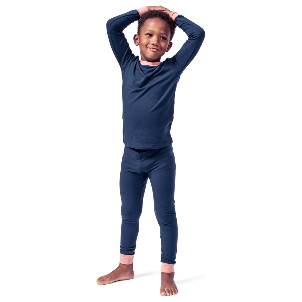 A child wearing a navy blue long-sleeve top and pants with pink ankle cuffs, standing with their hands raised and clasped.